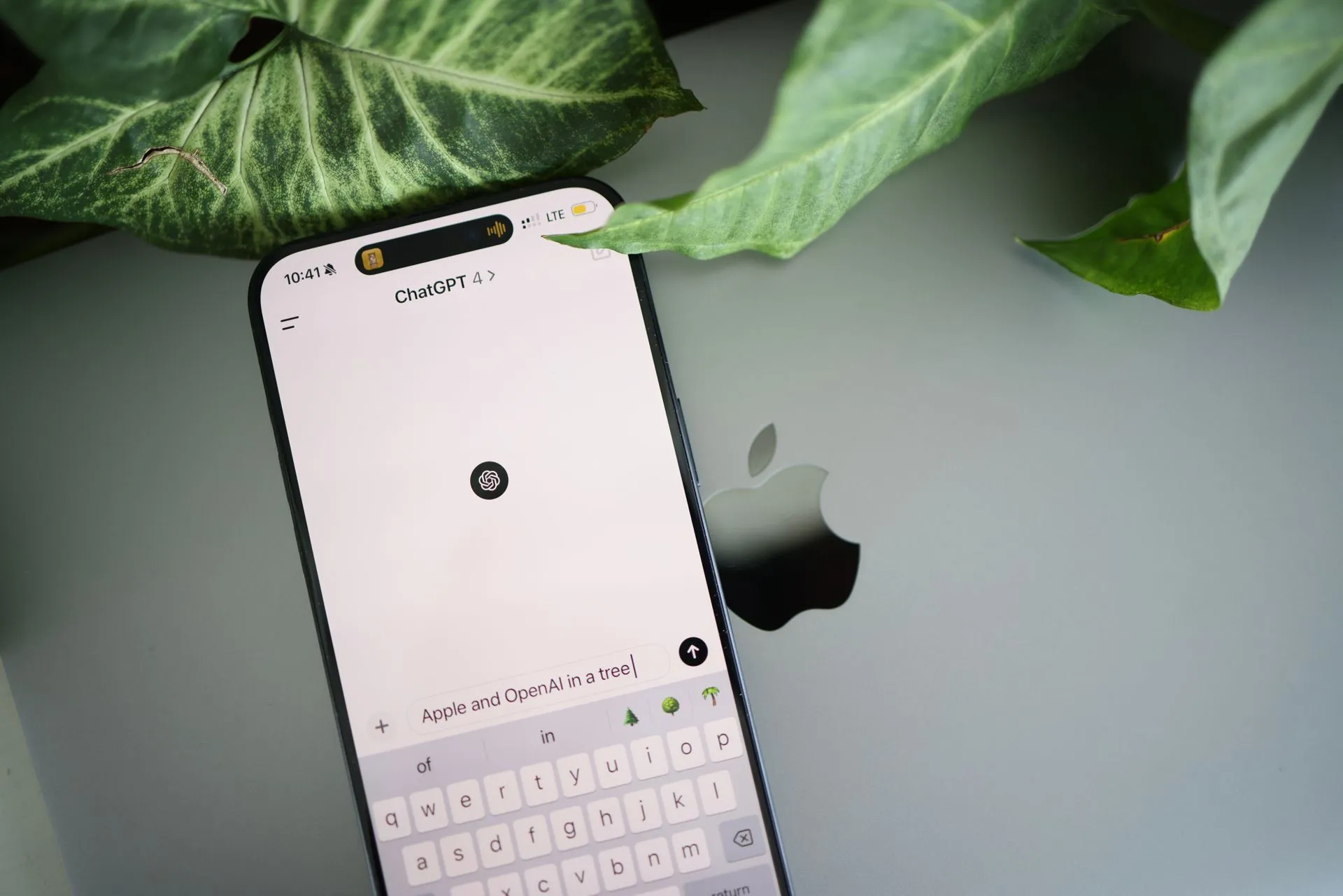 A smartphone shows a ChatGPT interface placed on an Apple laptop in a leafy environment, illustrating Salesforce's Agentforce Coworker reached 100,000 activated users in 35 days as AI